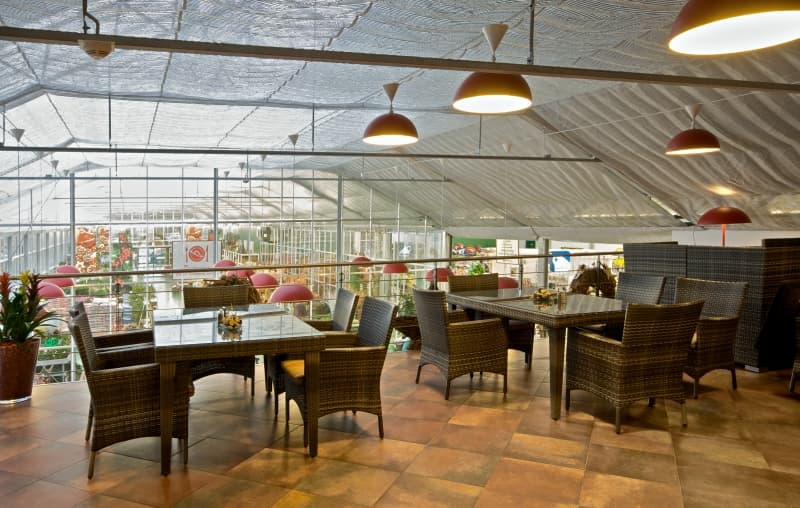 Jídelna Restaurace Chládek pod prosklenou skleníkovou střechou, stoly mezi rostlinami a červené závěsné lampy